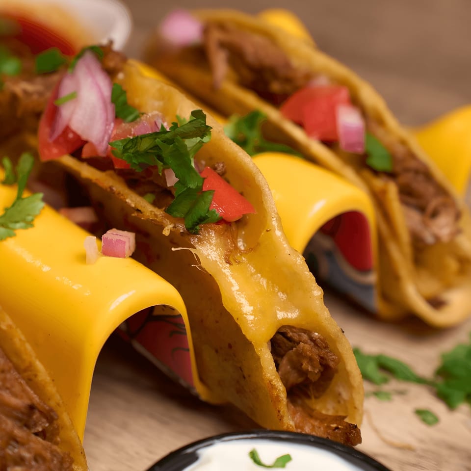 Three crispy tacos filled with meat, cheese, diced tomatoes, red onions, and cilantro.