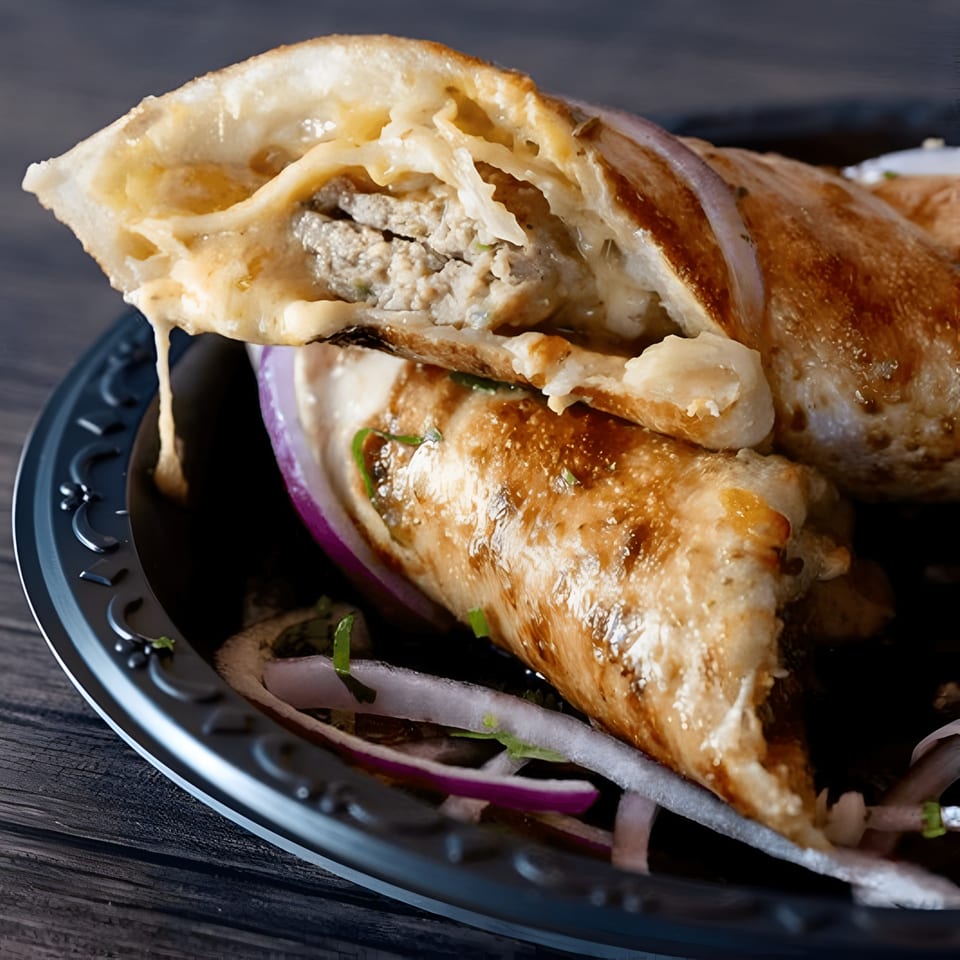 Close-up of a Pakistani chicken roll, revealing juicy meat, melted cheese, and red onions.