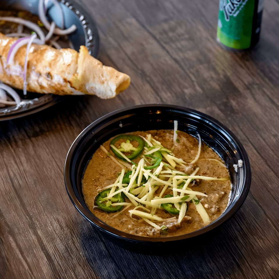 Pakistani haleem topped with ginger and green chilies, with a kebab roll in the background.