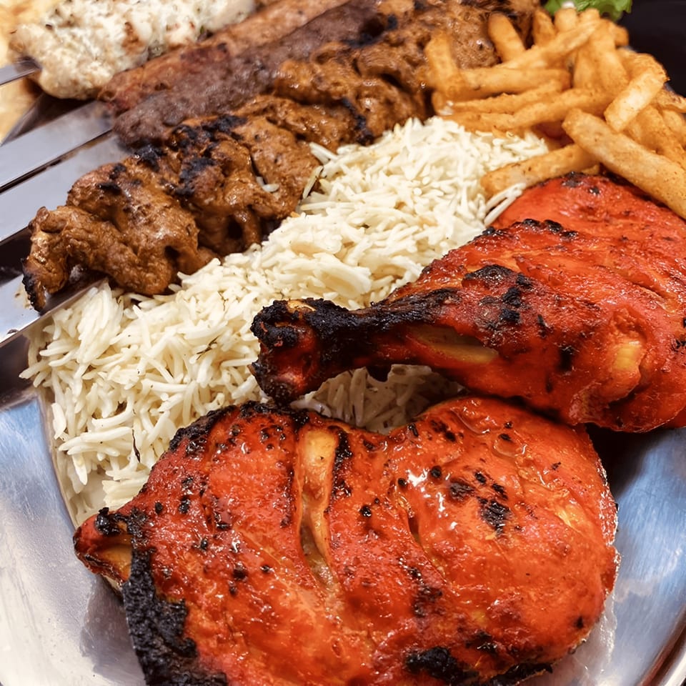 A platter of Pakistani food with tandoori chicken, rice, fries, and various kebabs.